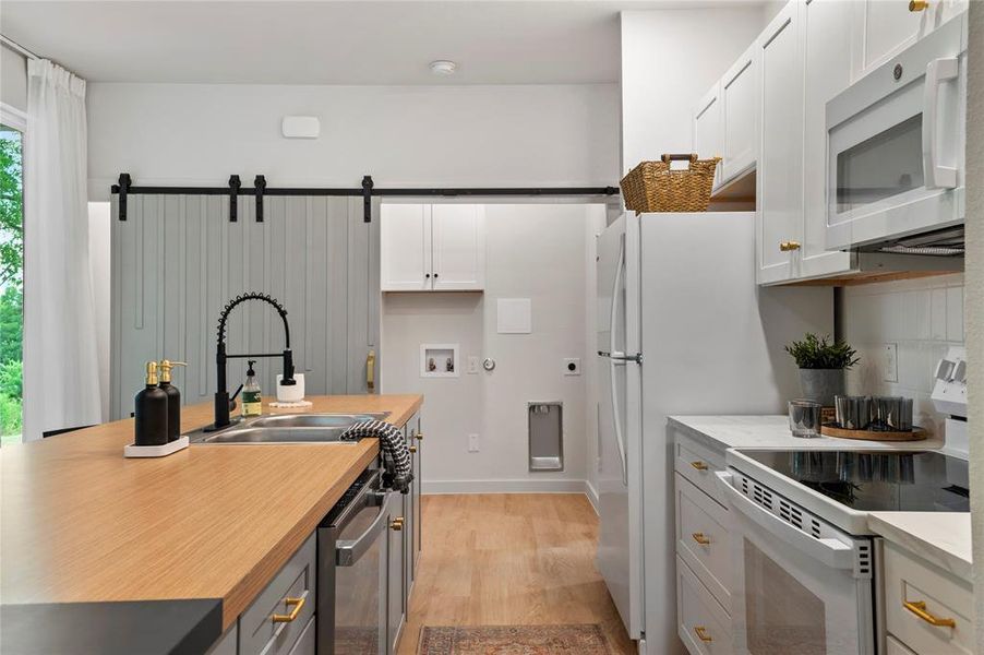 Kitchen with light hardwood / wood-style flooring, white appliances, sink, gray cabinets. Laundry behind barn door.