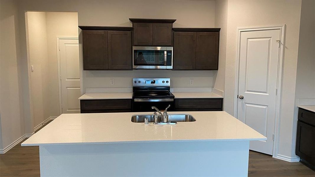 Kitchen with dark wood finish cabinets, stainless steel appliances, dark wood-style flooring, and a kitchen island with sink
