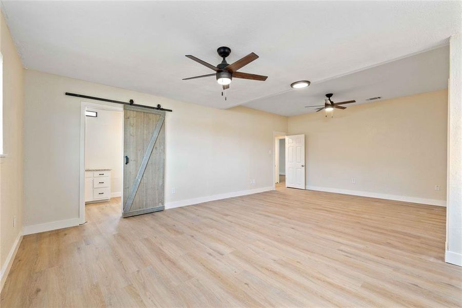 Empty room featuring a barn door, light wood-type flooring, and ceiling fan Empty room featuring a barn door, light wood-type flooring, and ceiling fan