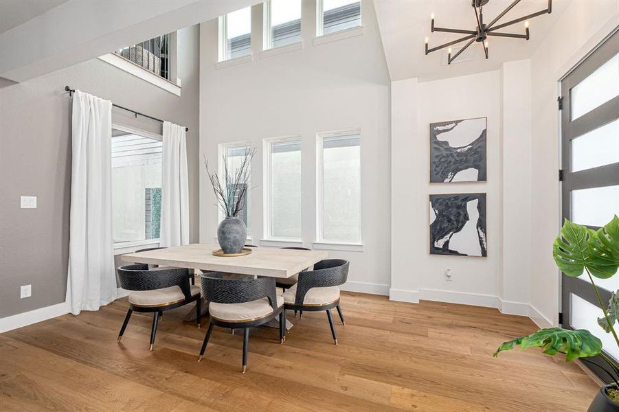Dining space featuring light wood-style flooring, a towering ceiling, and a chandelier