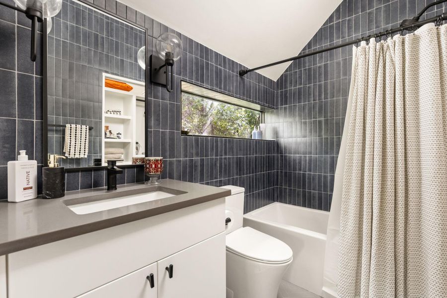 A refined bathroom features sleek dark tiling and a generous vanity, all illuminated by a discreet window. A refined bathroom features sleek dark tiling and a generous vanity, all illuminated by a discreet window.