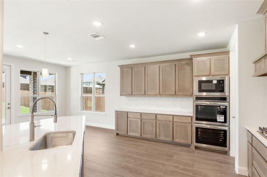 Kitchen with light wood cabinets, stainless steel double oven, built-in microwave, and white quartz island with sink