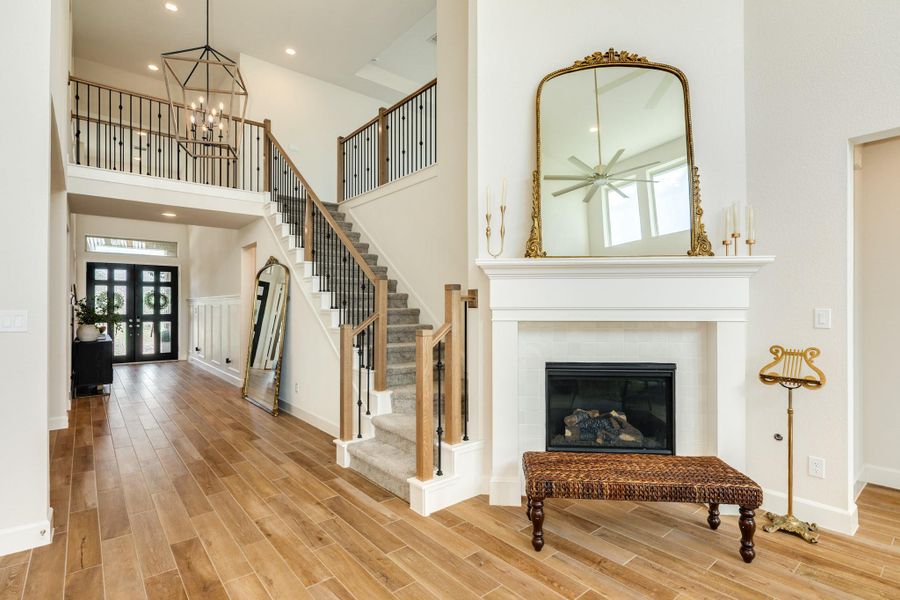 Stunning view from the family room looking toward the foyer, featuring an elegant staircase with custom wrought iron spindles and a modern statement chandelier. This inviting space is highlighted by a cozy corner gas fireplace and exquisite high-end flooring throughout. Stunning view from the family room looking toward the foyer, featuring an elegant staircase with custom wrought iron spindles and a modern statement chandelier. This inviting space is highlighted by a cozy corner gas fireplace and exquisite high-end flooring throughout.