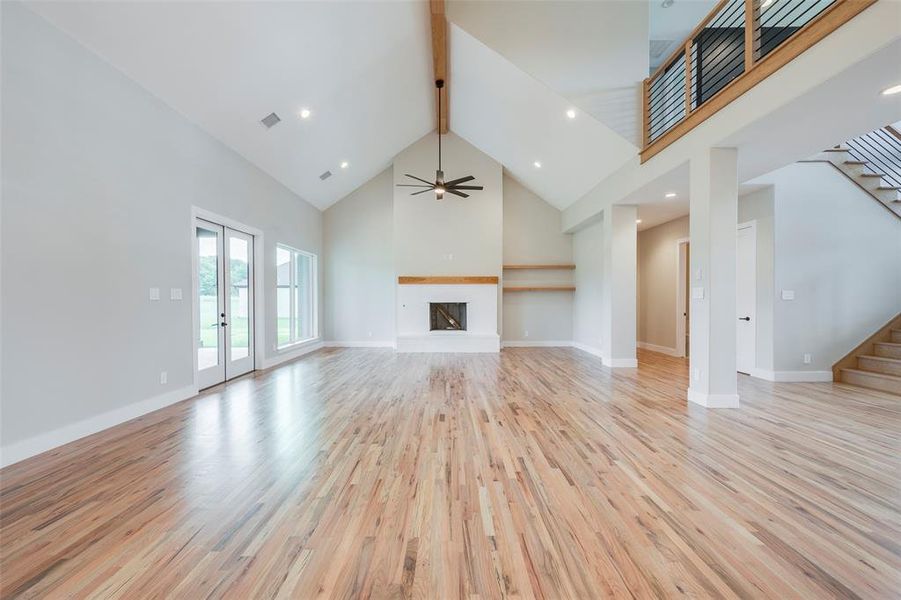 Unfurnished living room featuring high vaulted ceiling, beamed ceiling, a fireplace with raised hearth, light wood-style flooring, and stairway