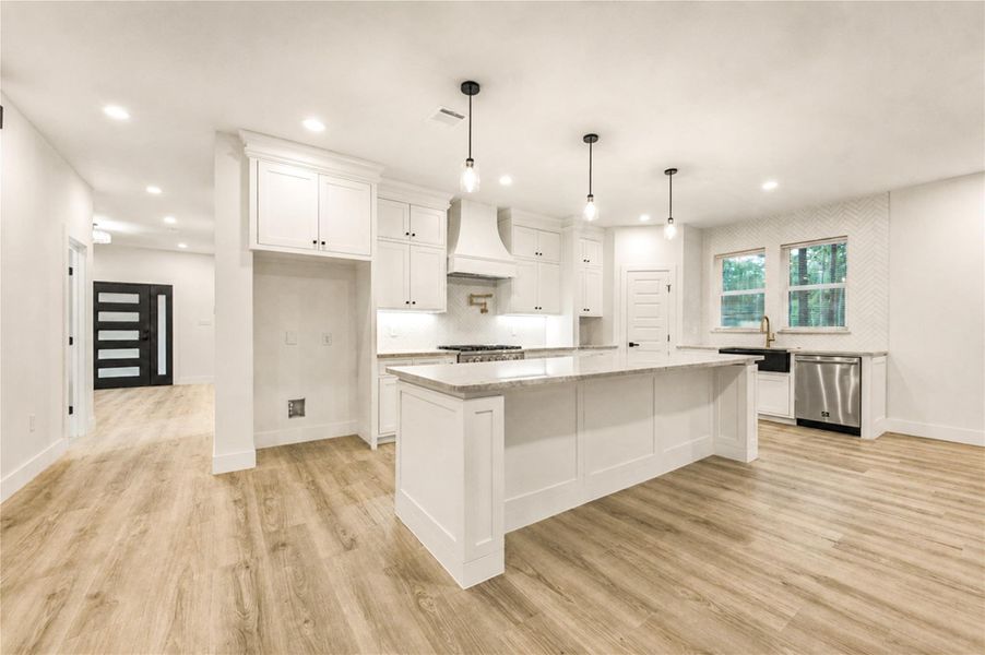 Stunning modern kitchen with sleek white cabinetry, a spacious island, and elegant pendant lighting, seamlessly flowing into an open-plan layout with beautiful LVP floors.