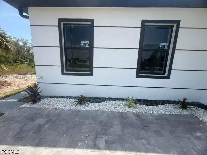 Exterior facade featuring white stucco finish with dark trim accents, double-hung windows, and paver hardscaping Exterior facade featuring white stucco finish with dark trim accents, double-hung windows, and paver hardscaping