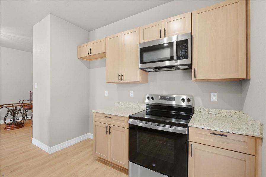 Kitchen featuring light wood finish cabinets, stainless steel appliances, light wood-type flooring, and light stone counters