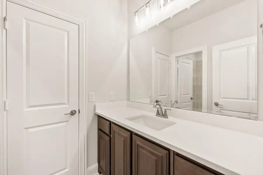 Bathroom vanity with dark wood cabinets, white countertop, single sink, and large mirror with overhead lighting