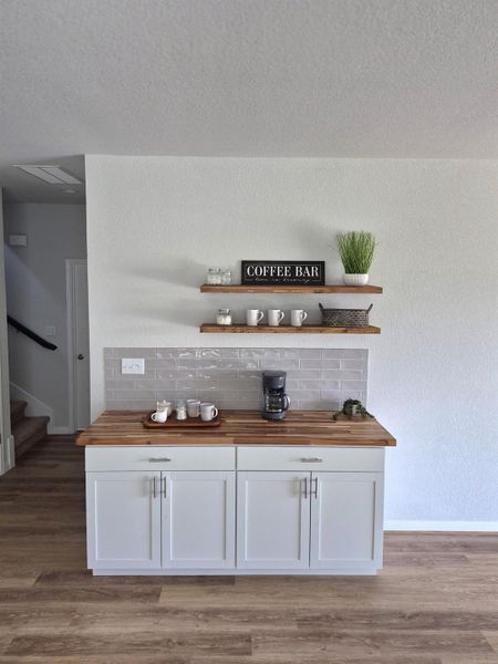 Bar area with butcher block countertops, open shelves, dark wood-style flooring, white cabinetry, and a textured wall