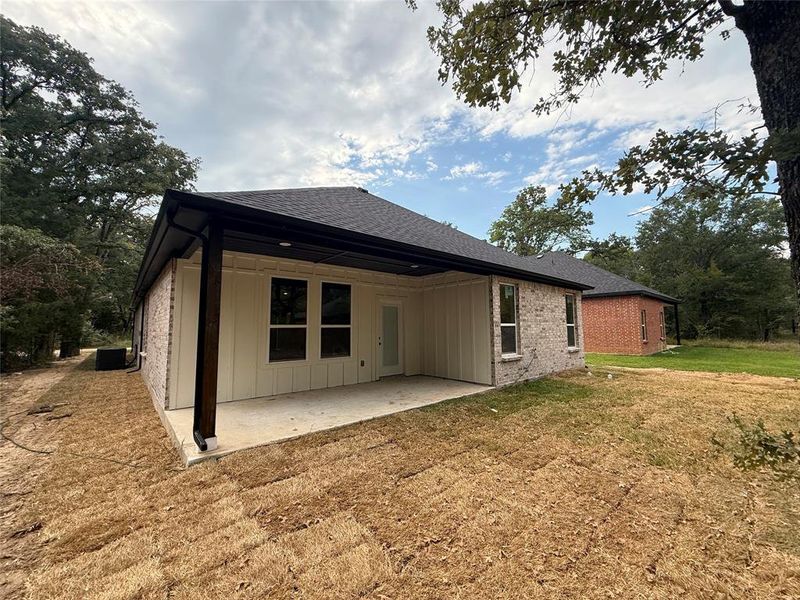Back of house featuring board and batten siding, a patio, brick siding, a lawn, and a shingled roof Back of house featuring board and batten siding, a patio, brick siding, a lawn, and a shingled roof