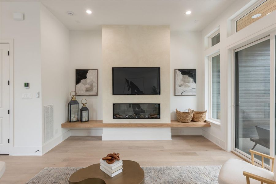 The fireplace wall as sculpture. A monolithic column of hand-troweled plaster climbs the full height of the space, flanked on either side by a floating white-oak hearth bench that reads as one continuous horizontal plane. The fire is long, low, and intentionally understated.