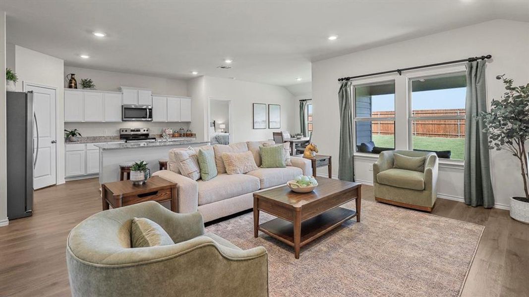 This open-concept living area features wood flooring, recessed lighting, and large windows that provide a view of the backyard