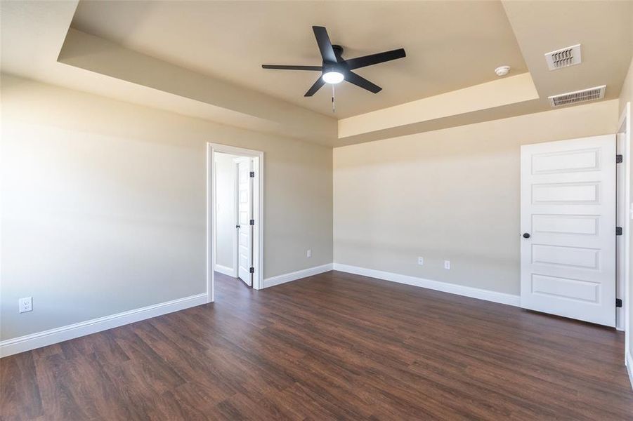 Spacious room featuring wood-finish flooring, a tray ceiling, and a ceiling fan with integrated lighting