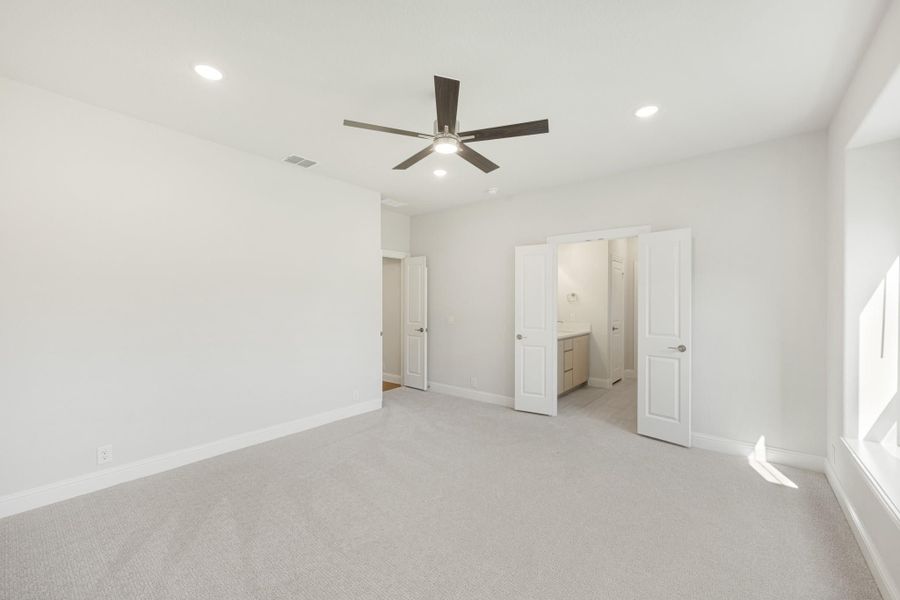 Empty bedroom with carpet, ceiling fan, and open doors leading to ensuite bathroom and closet
