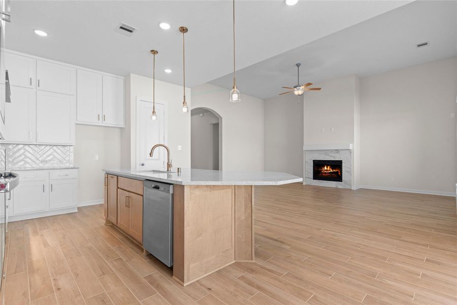 Another kitchen view emphasizes the open concept design, blending the kitchen and family room into one inviting gathering space, where wood like tile flooring, elegant lighting, and a warm fireplace create a truly welcoming atmosphere for hosting and relaxing.