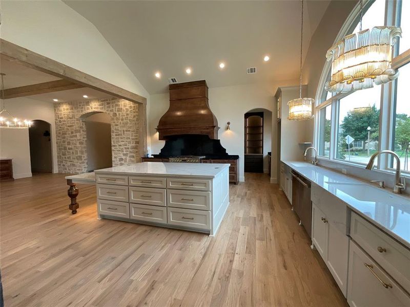 Kitchen featuring white cabinetry, light wood-type flooring, lofted ceiling, custom exhaust hood, and decorative light fixtures