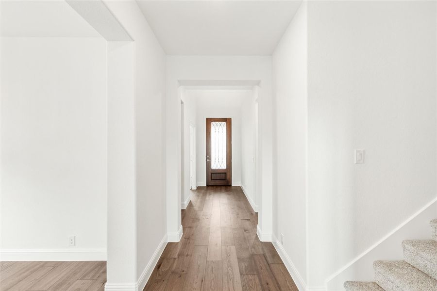 Hallway with wood floors, white walls, wood front door with glass panel, and staircase on the right
