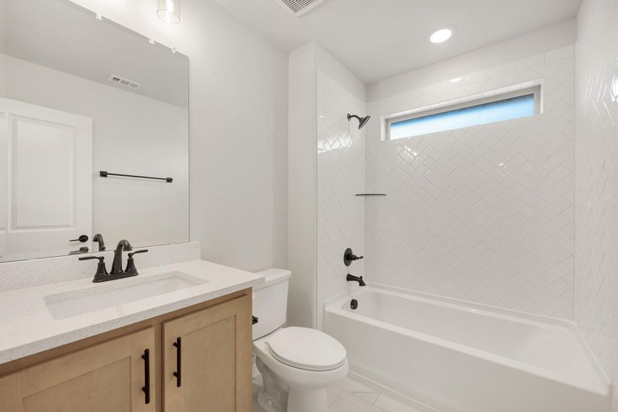 Bathroom with wood vanity, white quartz countertop, and tub-shower combo with white herringbone tile Bathroom with wood vanity, white quartz countertop, and tub-shower combo with white herringbone tile