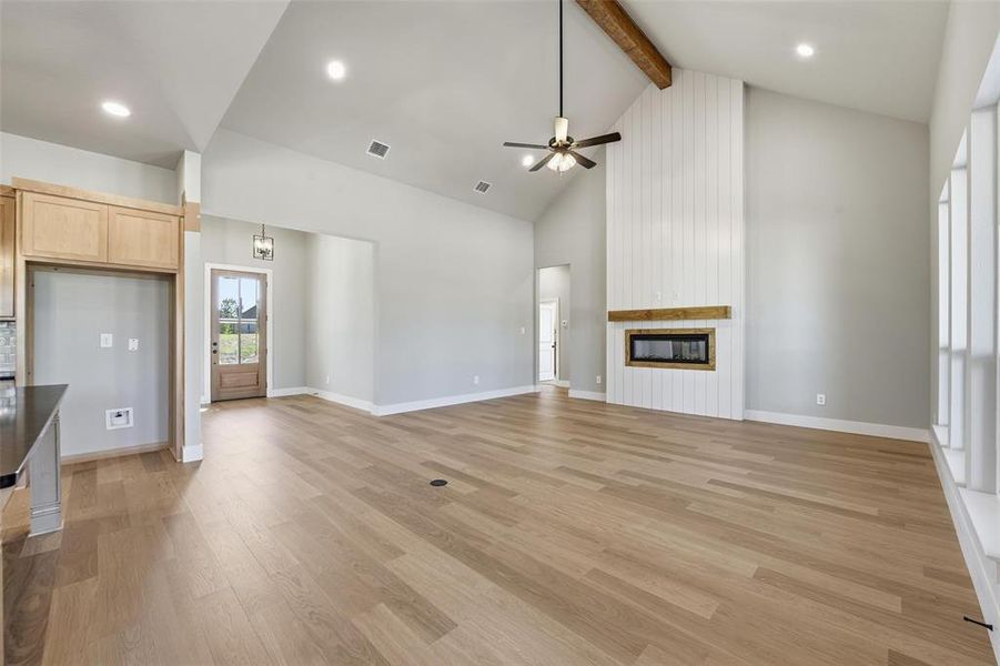 Unfurnished living room featuring light wood-style floors, beamed ceiling, high vaulted ceiling, ceiling fan, and a large fireplace