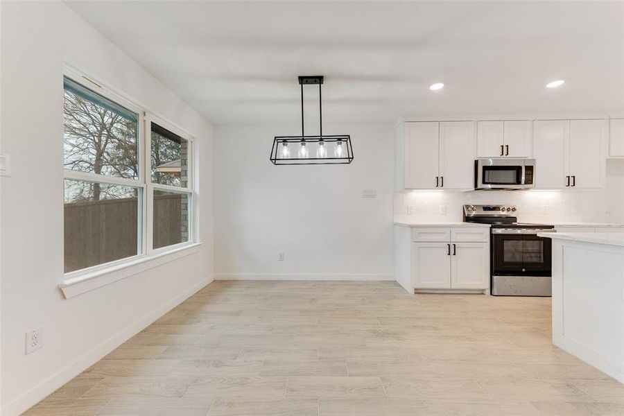 Kitchen featuring appliances with stainless steel finishes, backsplash, light hardwood / wood-style floors, white cabinets, and decorative light fixtures