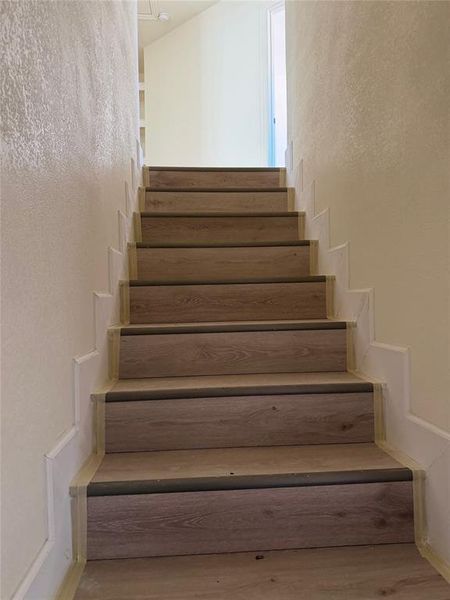Staircase with a textured wall and wood finished floors