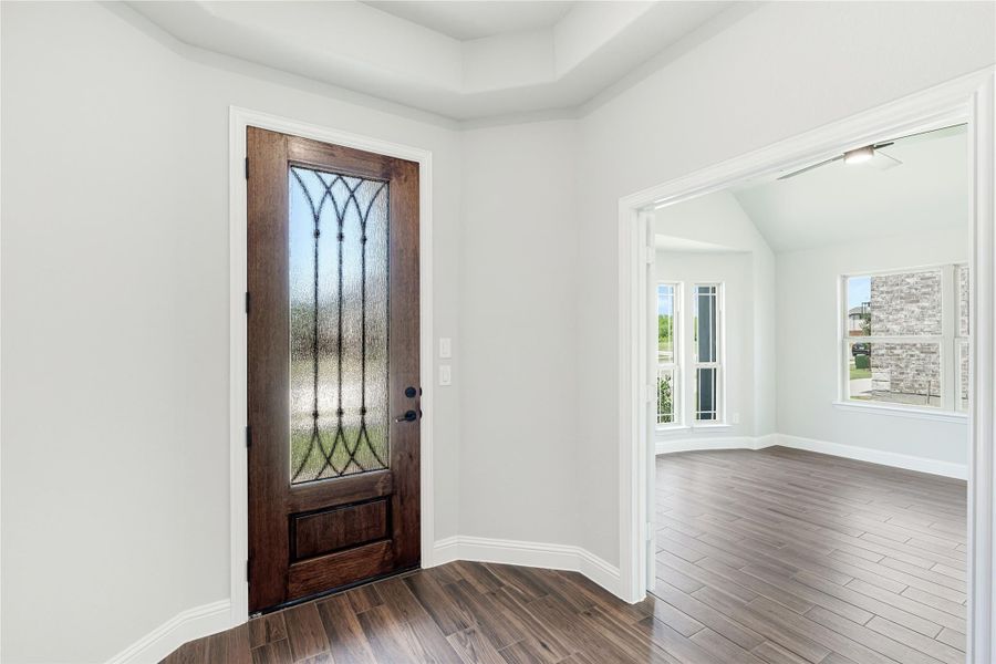 Entryway with dark wood front door featuring decorative glass panel and hardwood floors leading to an open room. Entryway with dark wood front door featuring decorative glass panel and hardwood floors leading to an open room.
