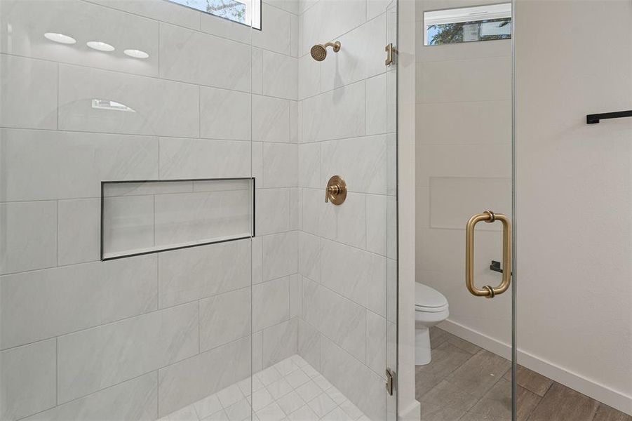 Walk-in shower featuring a frameless glass enclosure, white rectangular subway tile, integrated shower niche, and brass fixtures