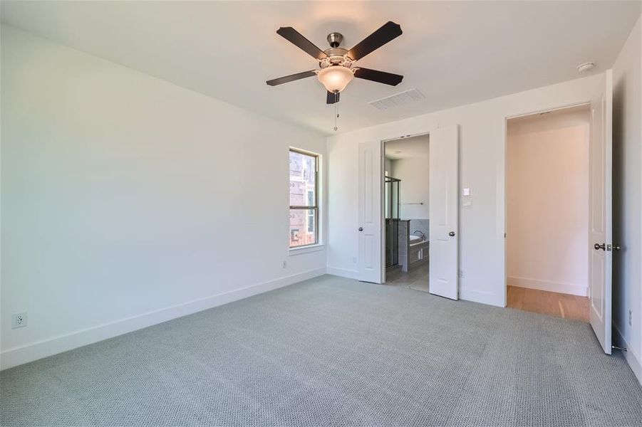 Unfurnished bedroom featuring light carpet, ensuite bathroom, and ceiling fan