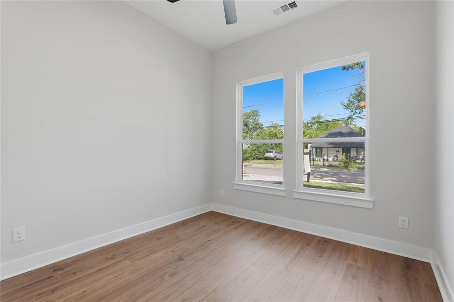 Bright interior space featuring two large windows, wood-finish flooring, white baseboards, and a ceiling fan Bright interior space featuring two large windows, wood-finish flooring, white baseboards, and a ceiling fan