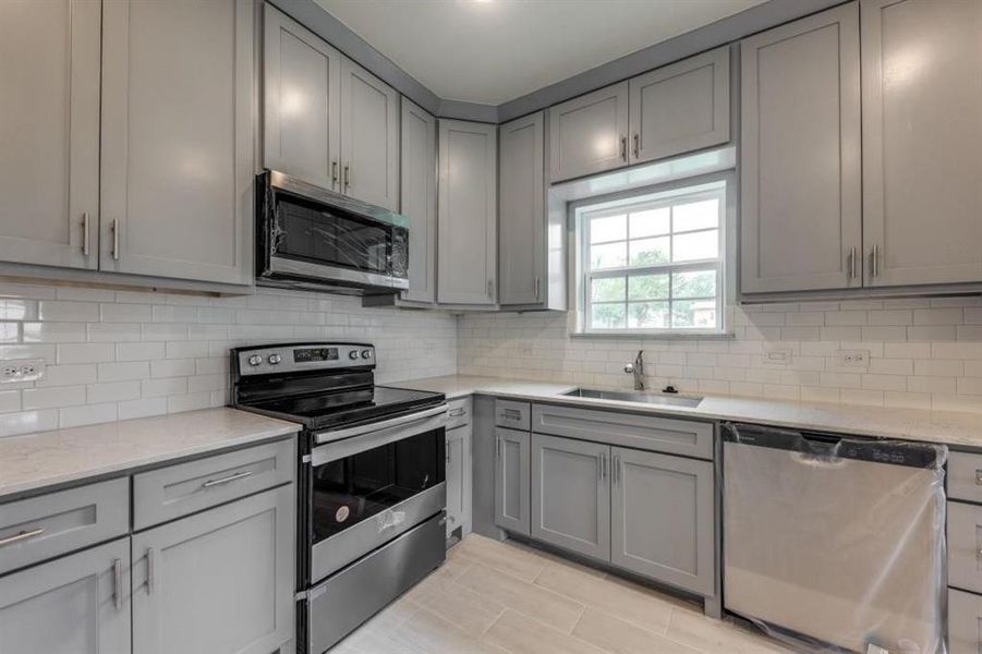 Kitchen featuring appliances with stainless steel finishes, sink, backsplash, and light tile flooring