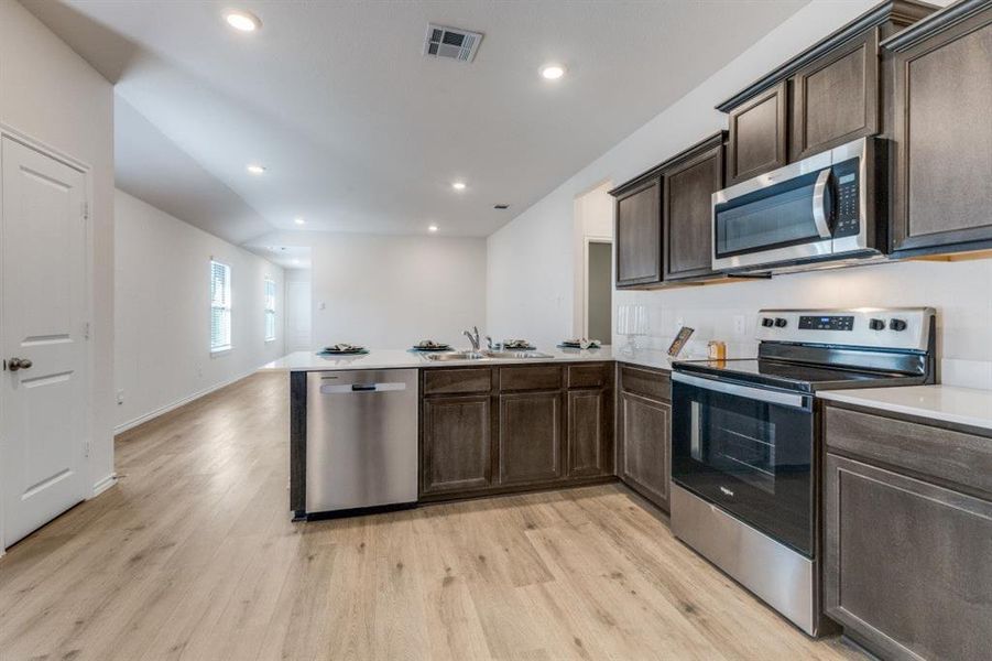 Kitchen with dark brown cabinetry, appliances with stainless steel finishes, a peninsula, light wood-style floors, and recessed lighting Kitchen with dark brown cabinetry, appliances with stainless steel finishes, a peninsula, light wood-style floors, and recessed lighting