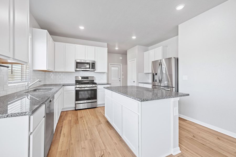 Kitchen featuring stainless steel appliances, light wood-style flooring, a center island, dark stone countertops, and white cabinetry Kitchen featuring stainless steel appliances, light wood-style flooring, a center island, dark stone countertops, and white cabinetry