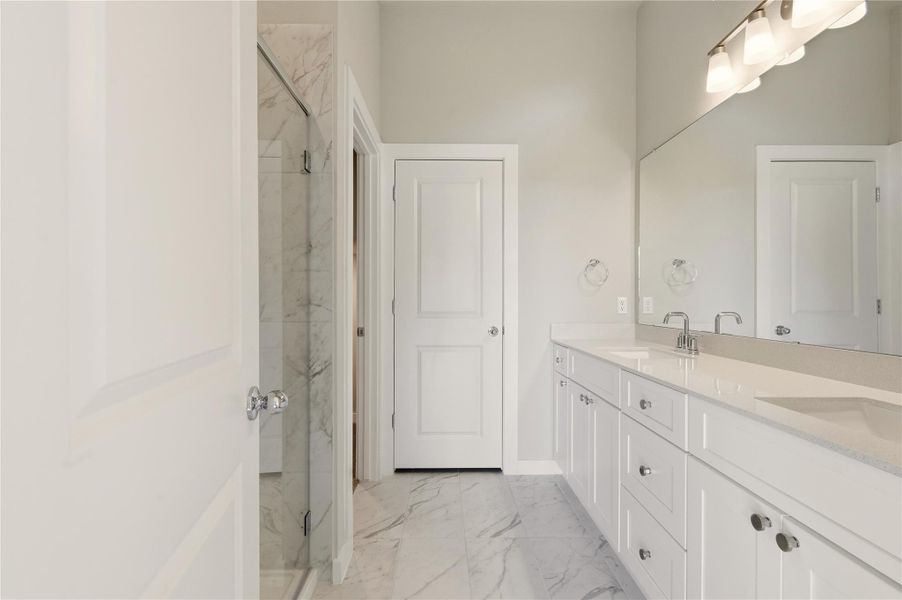 Bathroom featuring double vanity, light marble finish flooring, and a marble finish shower