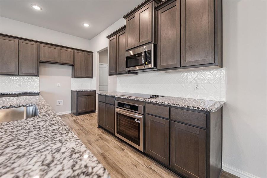 Kitchen featuring tasteful backsplash, light stone counters, dark brown cabinetry, stainless steel appliances, and recessed lighting Kitchen featuring tasteful backsplash, light stone counters, dark brown cabinetry, stainless steel appliances, and recessed lighting
