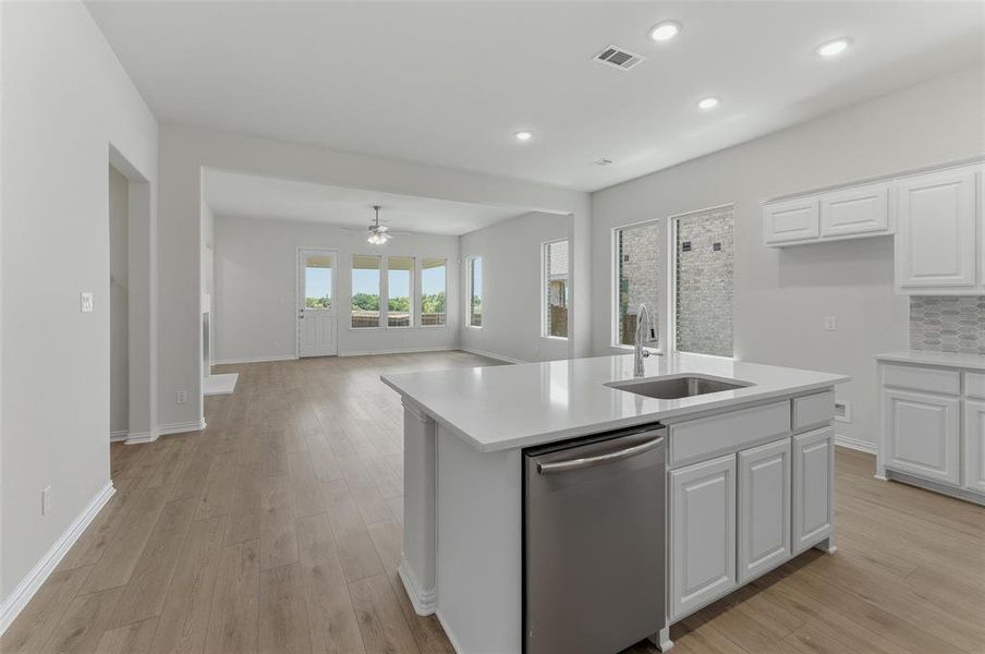 Open-concept living space featuring wood-finish flooring, recessed lighting, and a kitchen island with an integrated stainless steel sink and dishwasher Open-concept living space featuring wood-finish flooring, recessed lighting, and a kitchen island with an integrated stainless steel sink and dishwasher