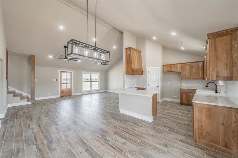 Kitchen with decorative backsplash, high vaulted ceiling, a ceiling fan, brown cabinets, and open floor plan Kitchen with decorative backsplash, high vaulted ceiling, a ceiling fan, brown cabinets, and open floor plan
