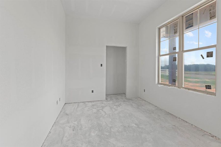 Spacious room featuring a large multi-pane window, an open doorway, neutral wall finishes, and a raw concrete floor Spacious room featuring a large multi-pane window, an open doorway, neutral wall finishes, and a raw concrete floor