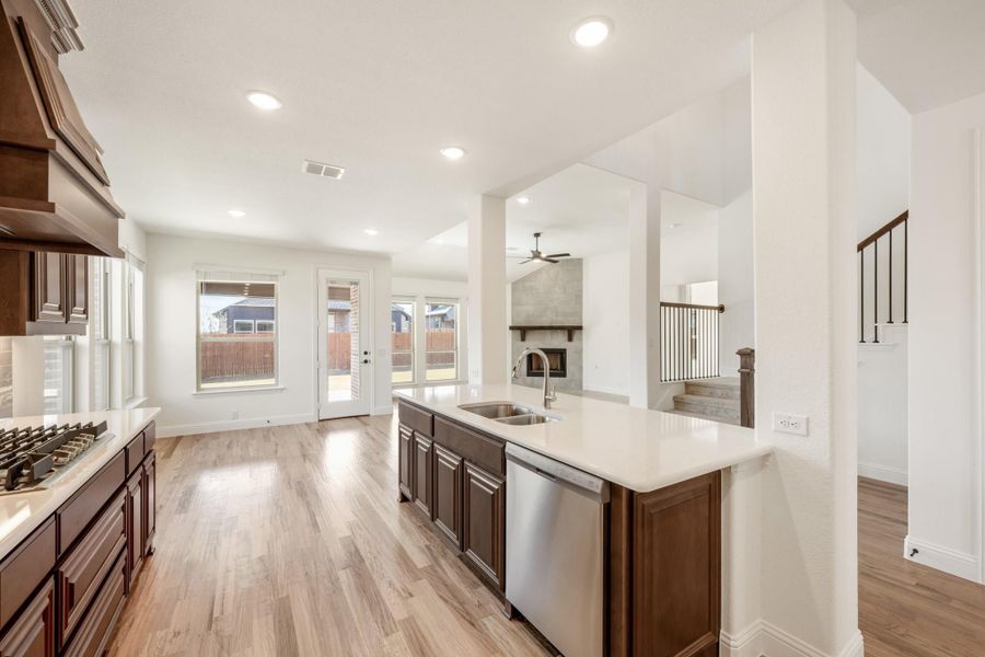 Kitchen with dark wood cabinets, white countertops, and island sink open to living area with fireplace