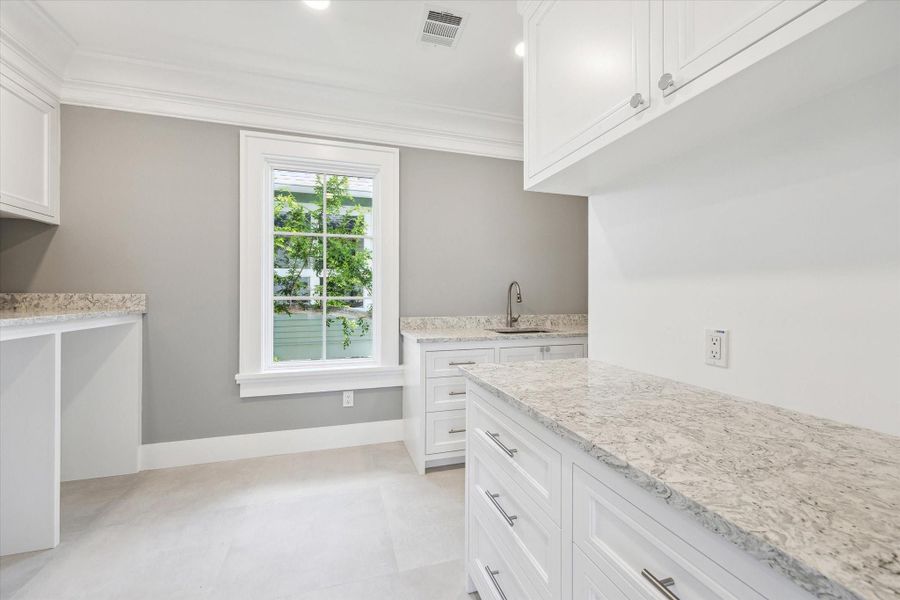 This second floor room features a bright and spacious laundry and utility area with ample white cabinetry, hard-surface countertops, and a large window providing natural light.