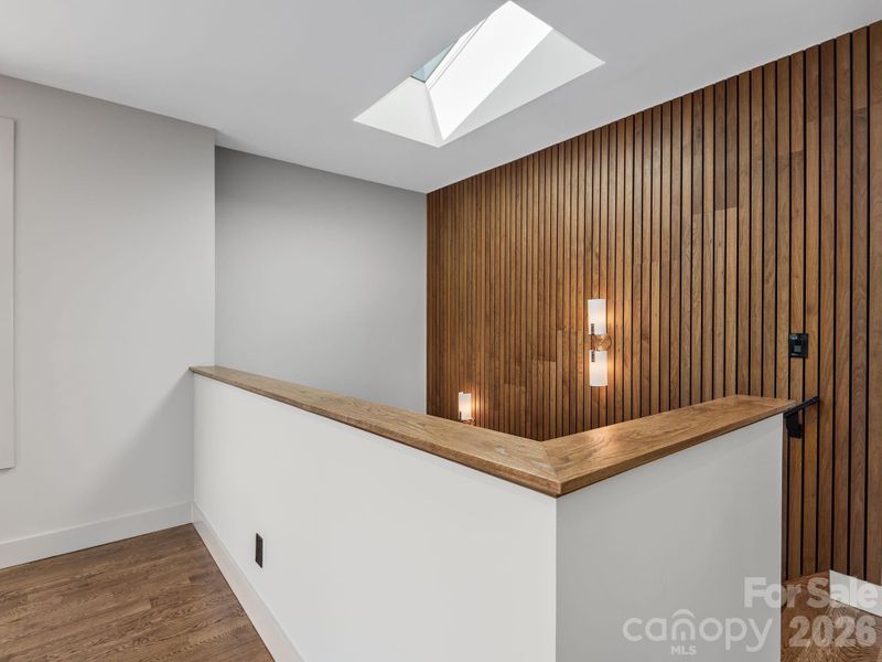Representative photo from 50 Verde Drive showing the builder’s quality of construction and finish level, including the stairwell with oak handrail detail, designer lighting, skylight above, and striking wood accent wall.