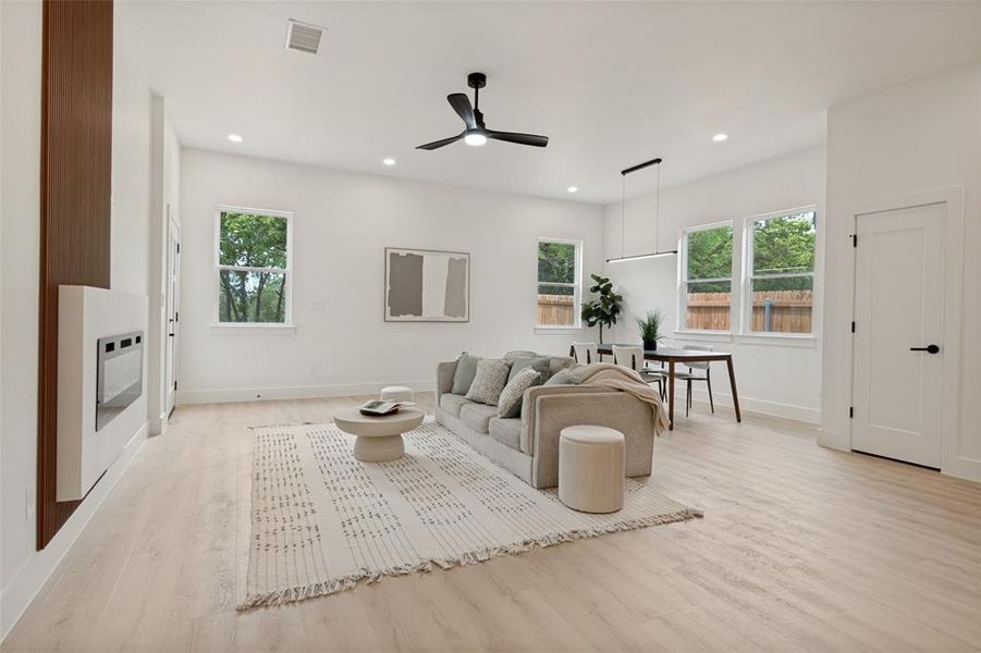 Open-concept living and dining area featuring light wood-finish flooring, recessed lighting, and multiple windows