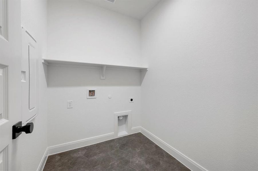 Dedicated laundry area featuring a built-in wall shelf, dark hexagonal floor tiles, white baseboards, and a paneled door with a black knob