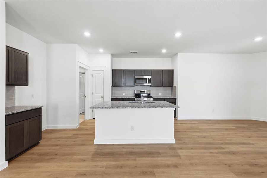 Kitchen featuring light stone countertops, dark wood finish cabinetry, a kitchen island with sink, light wood-type flooring, and recessed lighting