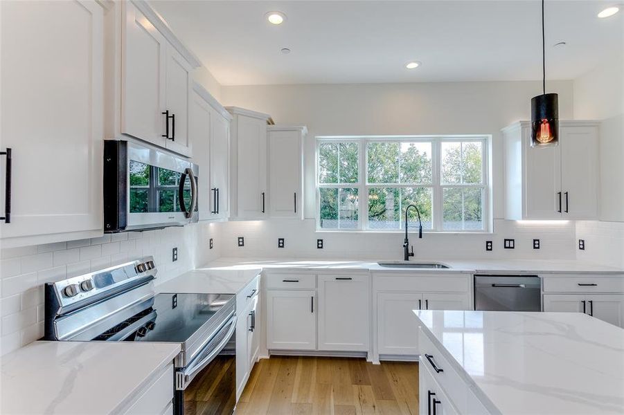 Kitchen with stainless steel appliances, sink, decorative light fixtures, light hardwood / wood-style floors, and white cabinetry