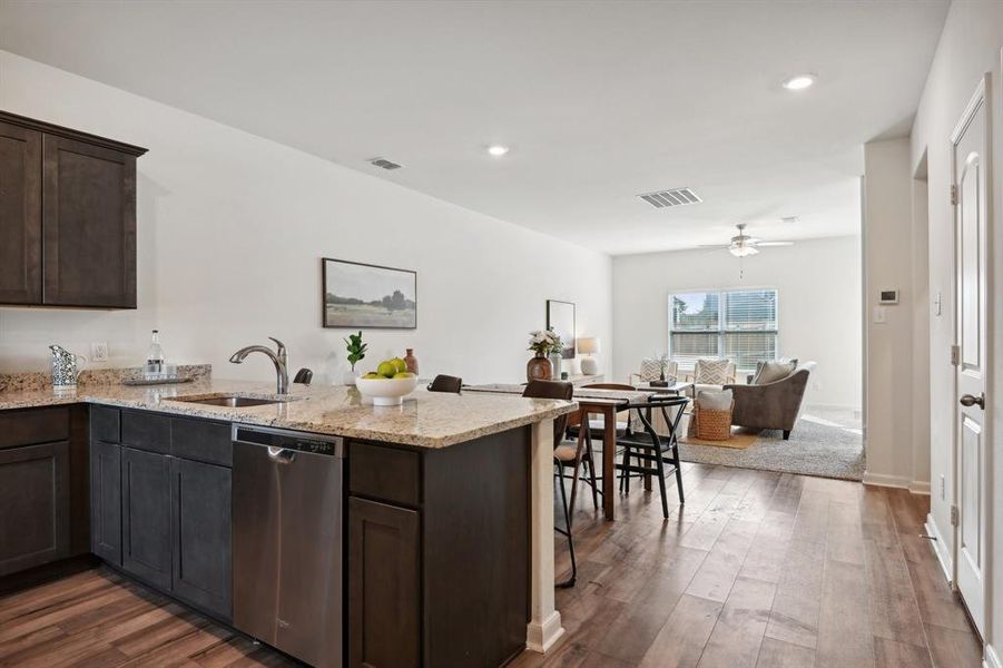 Kitchen with dark wood-type flooring, kitchen peninsula, light stone countertops, dishwasher, and sink