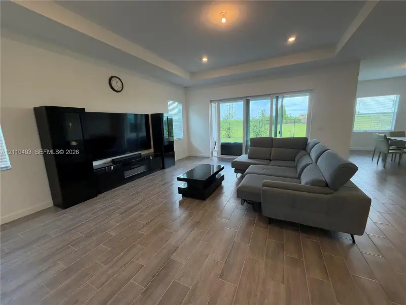 Living area featuring tray ceilings, recessed lighting, wood-finish tile flooring, and large sliding glass doors