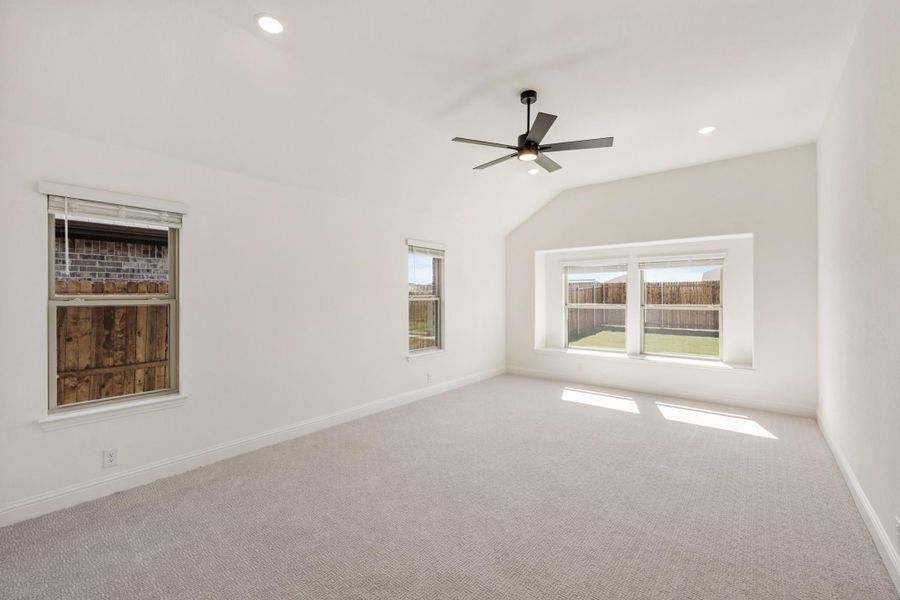 Empty bedroom with vaulted ceiling, ceiling fan, carpet flooring, and multiple windows with backyard views Empty bedroom with vaulted ceiling, ceiling fan, carpet flooring, and multiple windows with backyard views