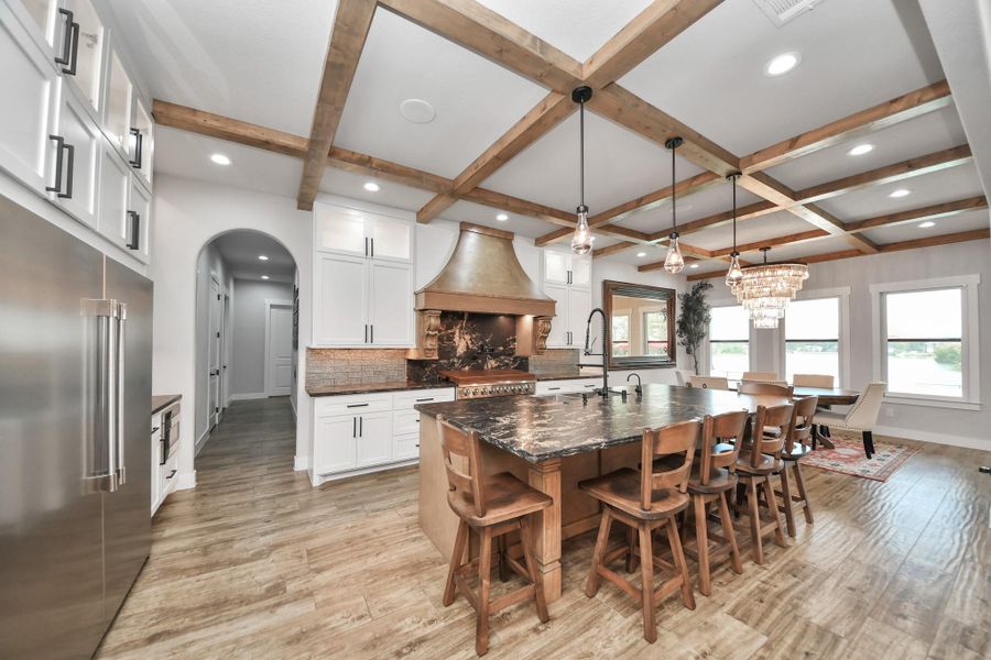 Stunning kitchen with a spacious island, elegant pendant lighting, and exposed wood beam ceiling, seamlessly flowing into a bright dining area with large windows.