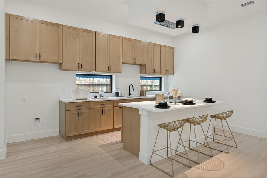 Kitchen featuring a central island with white countertop, extensive light wood cabinetry, recessed lighting, and wood-finish flooring
