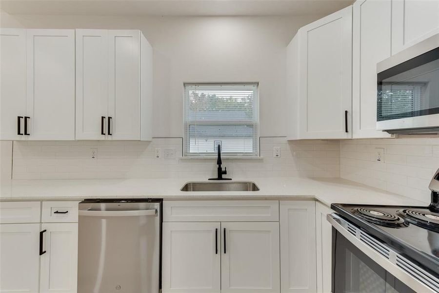 Kitchen featuring backsplash, sink, appliances with stainless steel finishes, and white cabinetry